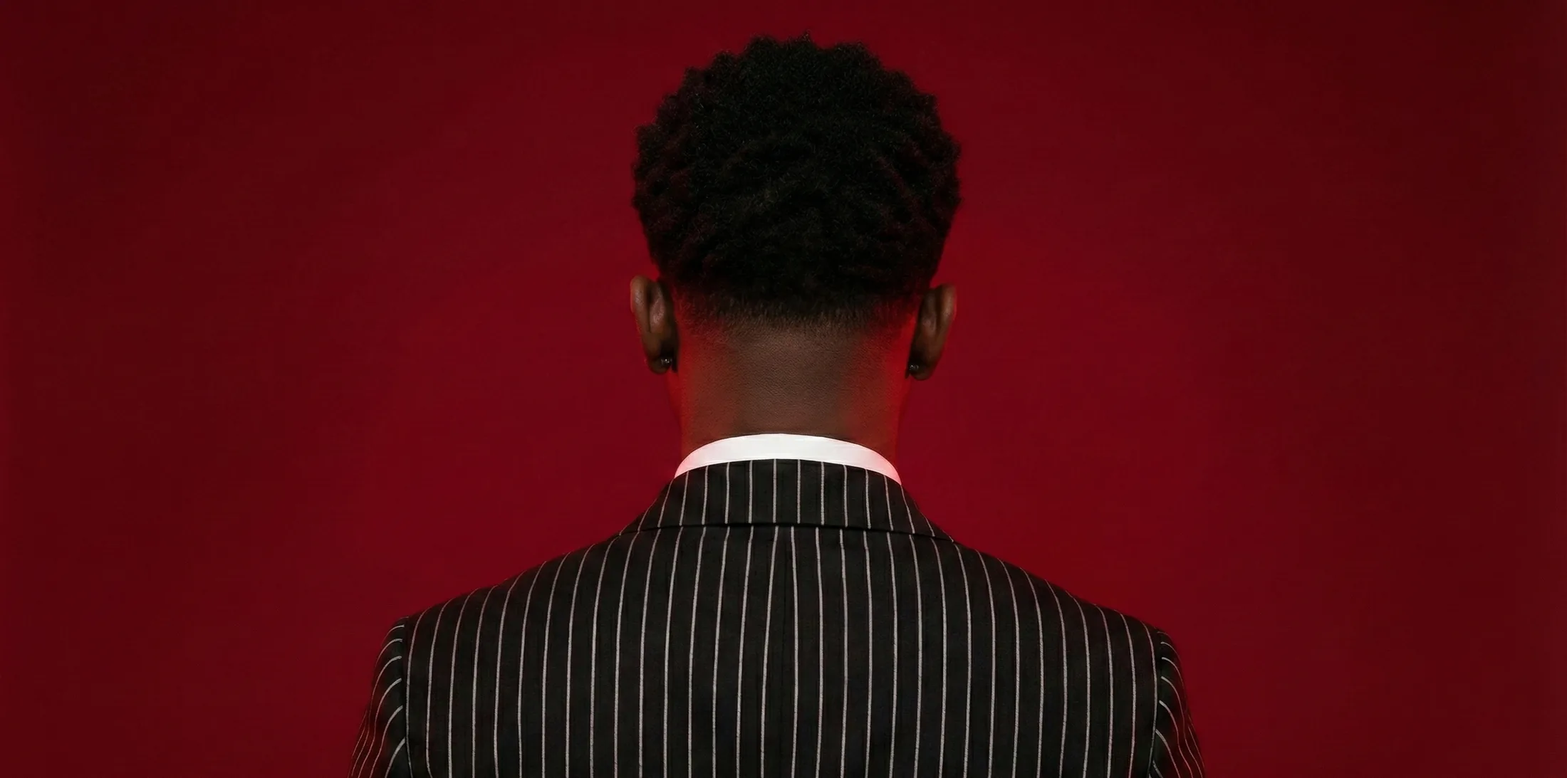 Siyanda Lembethe, seen from behind in a pinstripe jacket against a deep red backdrop